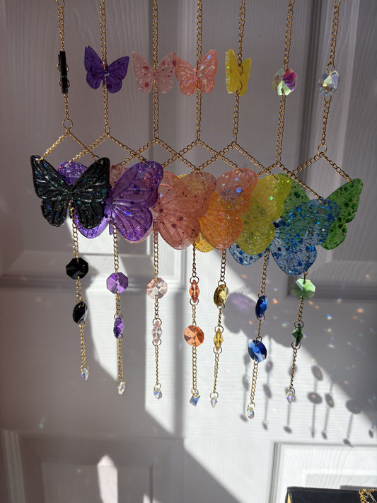 Colorful butterfly mini sun catchers with resin and crystal designs, hanging on gold chains, creating vibrant light reflections.